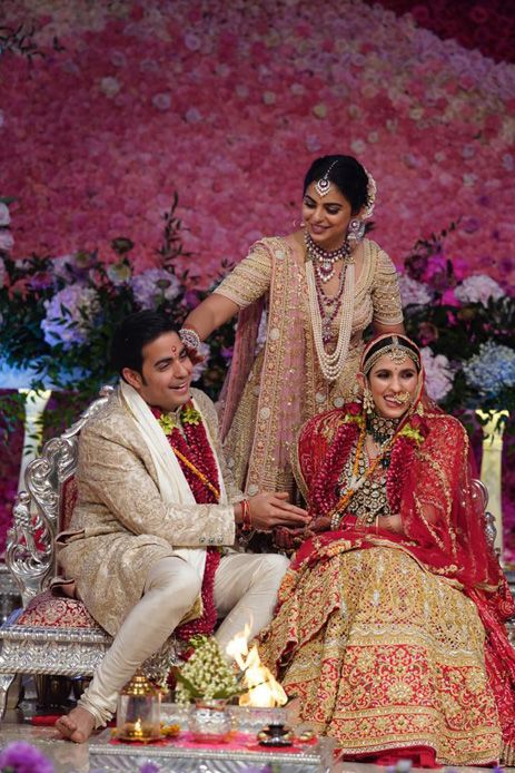 a bride and groom sitting on a bench in front of a flowered wall with candles