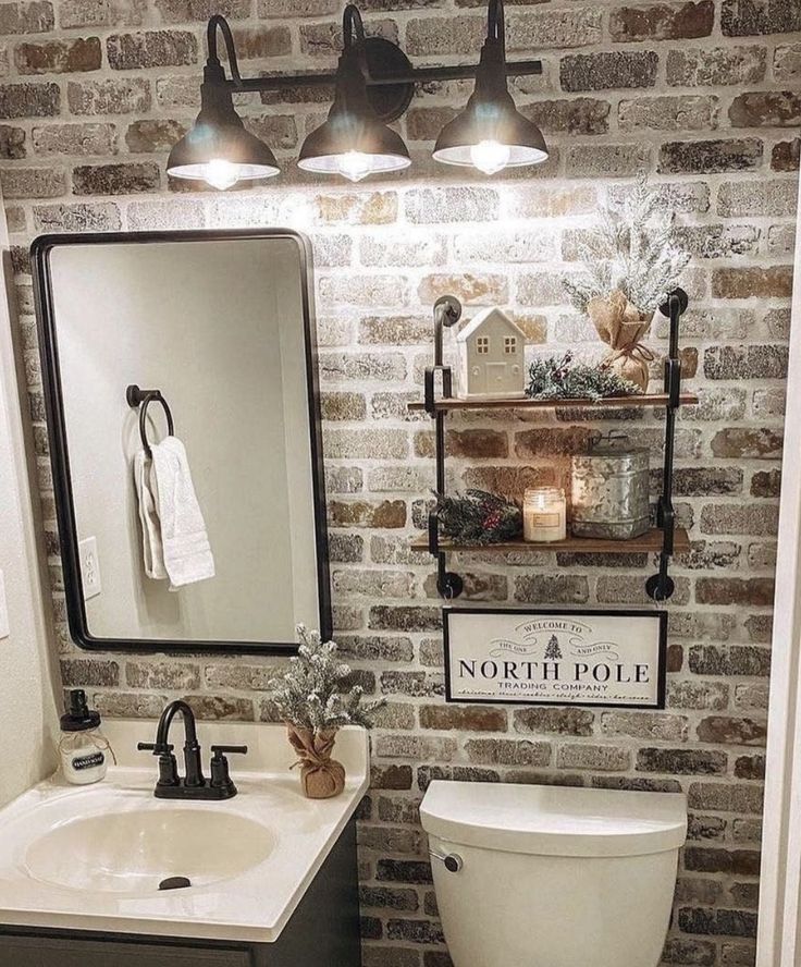 a white toilet sitting next to a sink in a bathroom under two lights on a brick wall