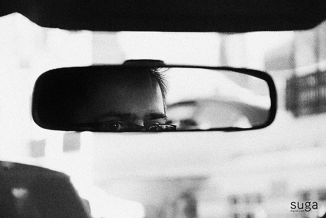 a man looking out the window of a car in front of another person's side view mirror