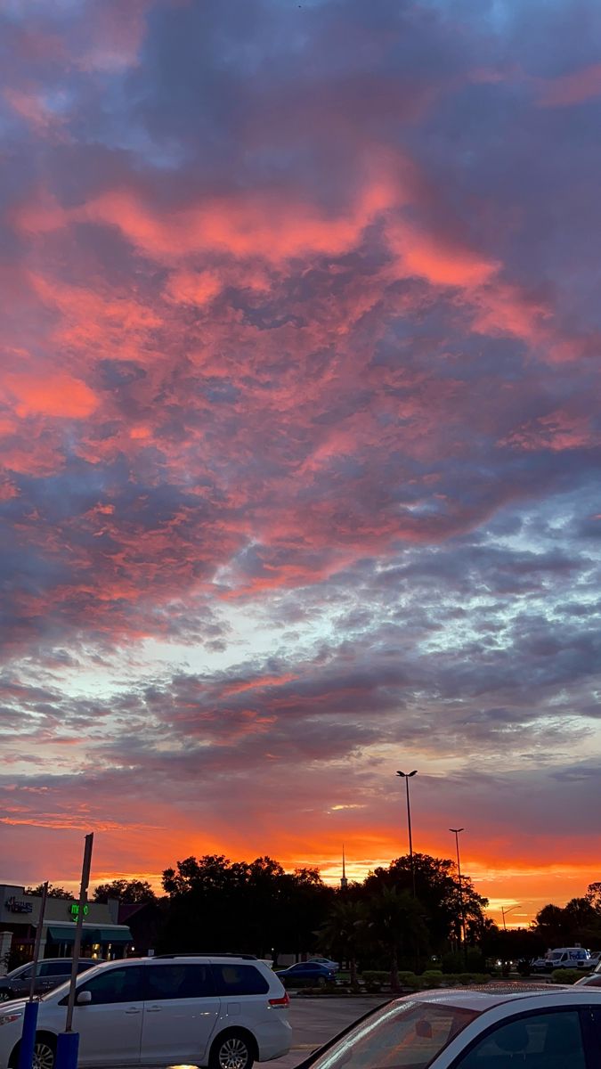 cars parked in a parking lot under a pink sky with clouds at sunset or dawn