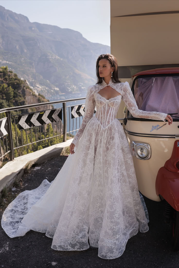 a woman standing next to an old car wearing a white wedding dress with long sleeves