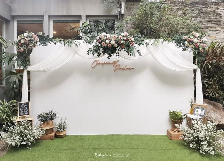 a white backdrop with flowers and greenery on the side for an outdoor wedding ceremony