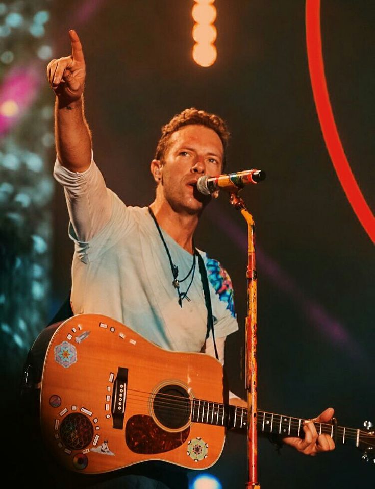 a man holding a guitar and giving the peace sign with his right hand while singing into a microphone