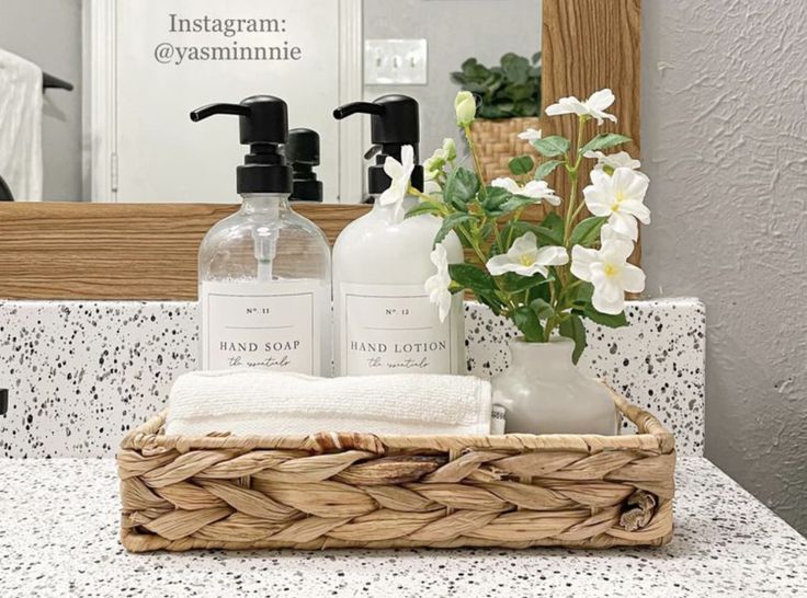 a bathroom counter with soap, lotion and flowers in a basket next to a mirror