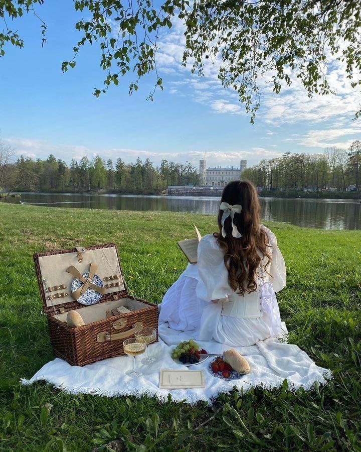 a woman sitting on top of a grass covered field next to a basket filled with food