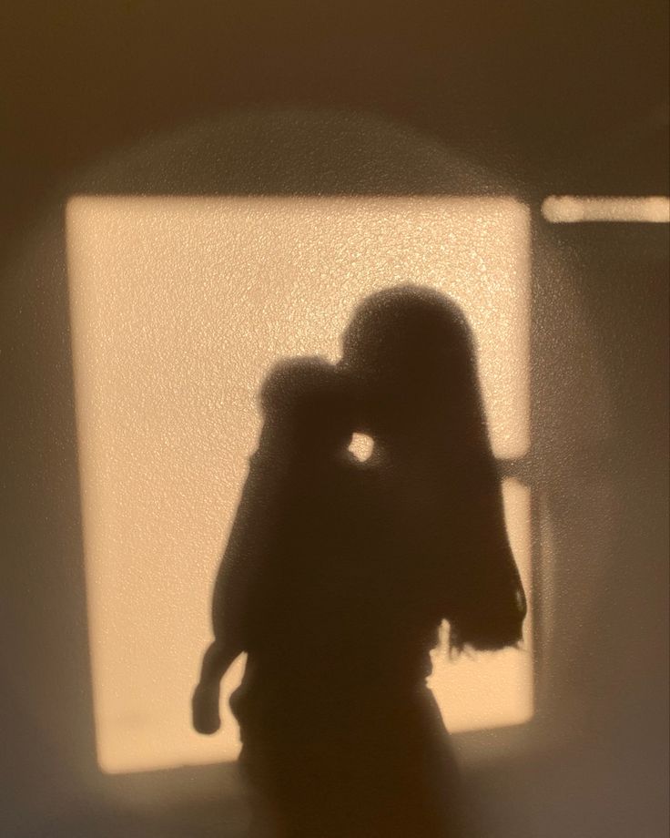 the shadow of a person holding a cell phone up to their face in front of a window