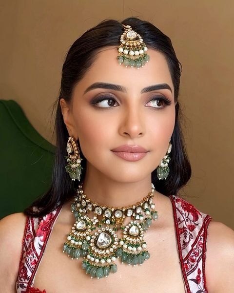 a woman in a red dress with green jewelry on her neck and headpieces