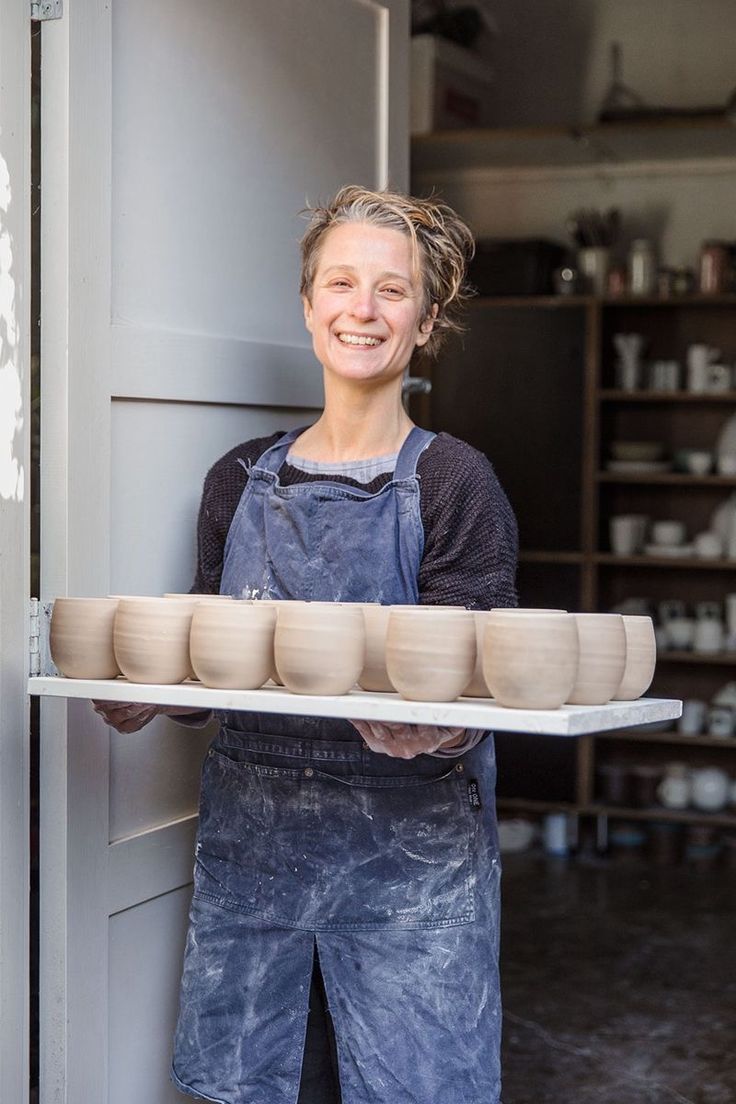 a woman holding a tray with bowls on it in front of a door and shelves