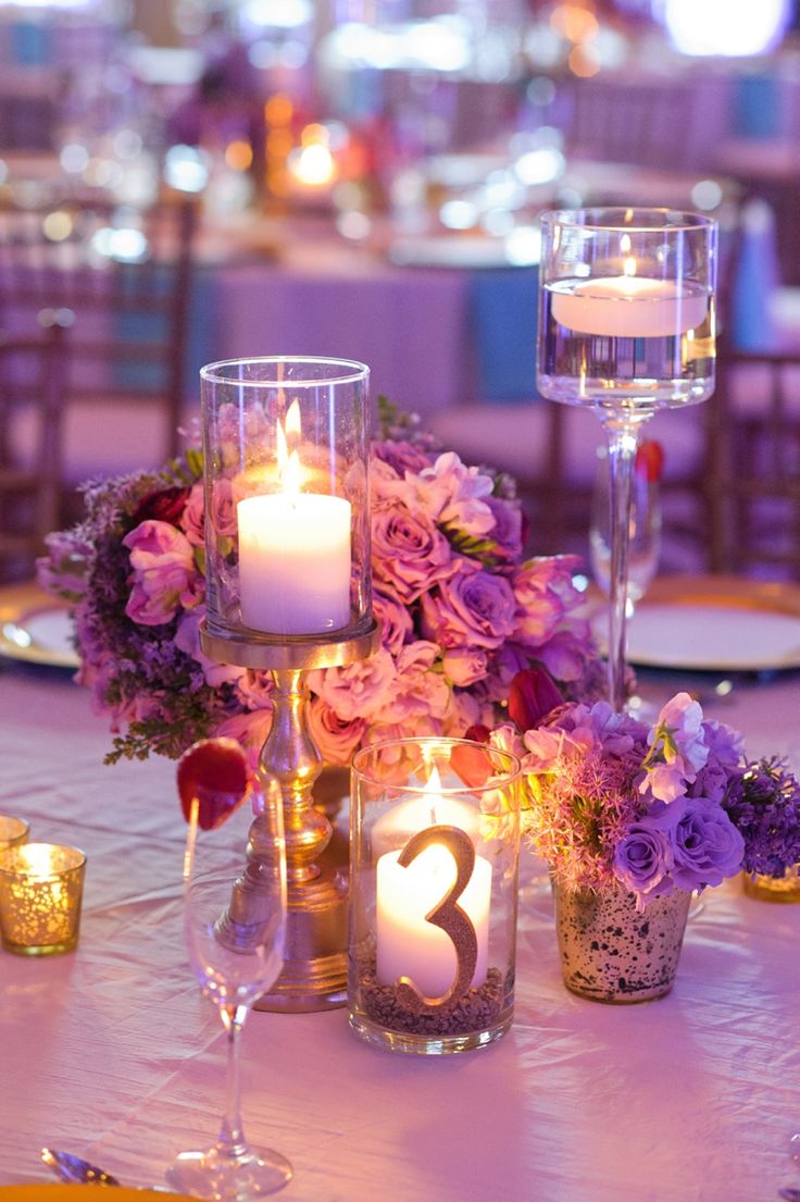 the centerpieces on this table are filled with purple flowers and greenery, along with candles