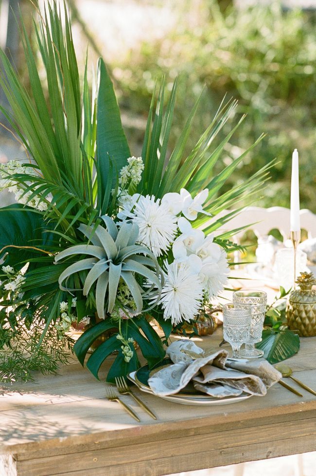 the table is set with white flowers and greenery on it, along with pineapples