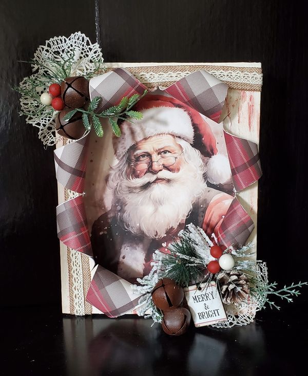 a christmas card with a santa clause on it and pine cones around the edges, sitting on a black surface