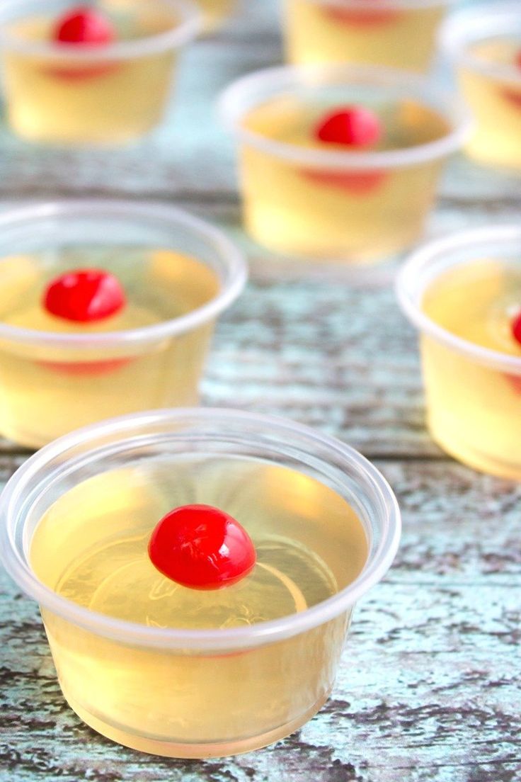 small plastic cups filled with yellow liquid and a cherry on the top, sitting on a table