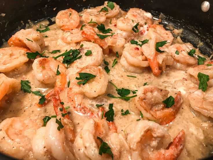 a skillet filled with shrimp and grits covered in gravy, garnished with parsley