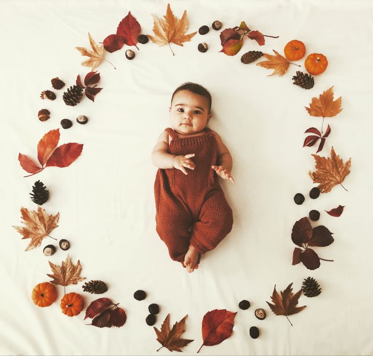 a baby laying in a circle surrounded by leaves and acorns