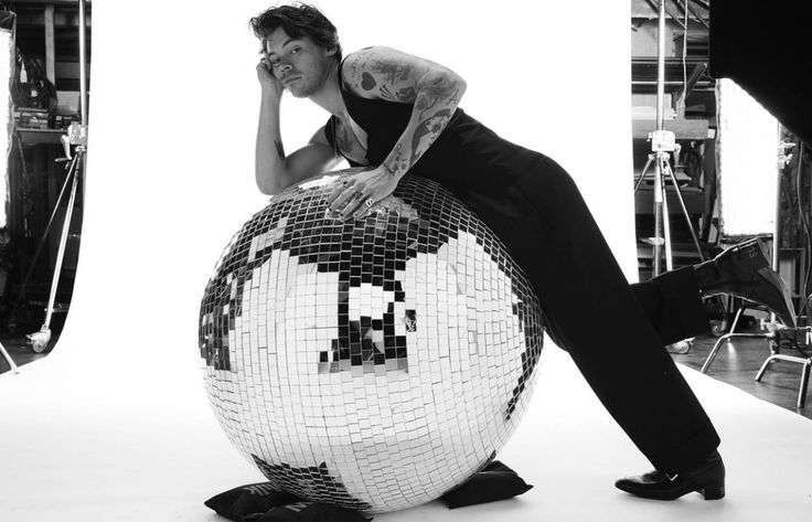 a man leaning on a disco ball in front of a white background with black and white images