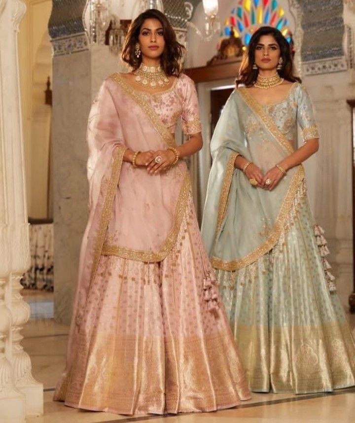 two women standing next to each other in matching outfits, one wearing a pink and blue lehenga