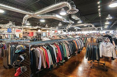 the inside of a clothing store with lots of clothes on racks and hanging lights above