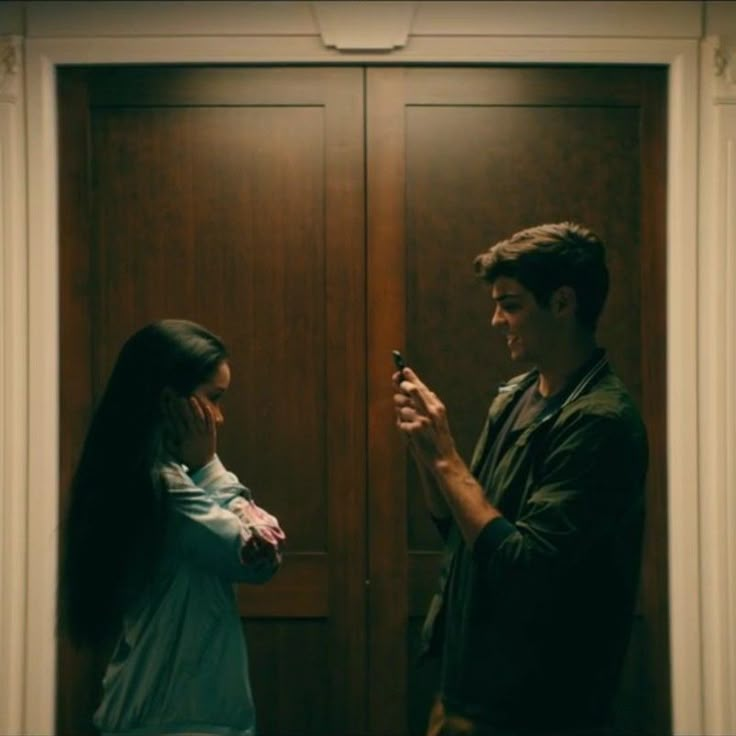 a man standing next to a woman in front of a door holding a cell phone