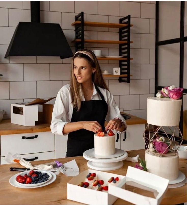 a woman in an apron is decorating a cake with strawberries and raspberries