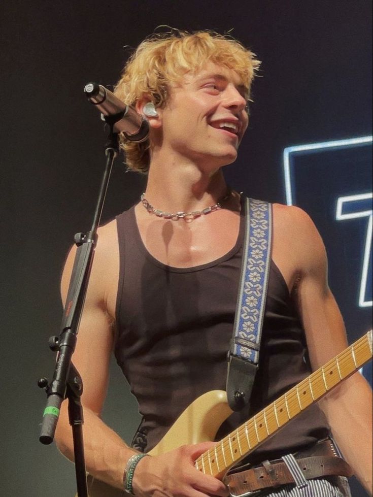 a man that is standing in front of a microphone with a guitar on his chest