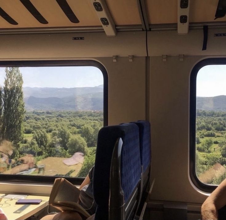 two people are sitting on a train looking out the windows at trees and mountains in the distance