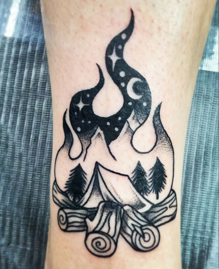 a black and white tattoo on the leg of a person with a campfire in the background