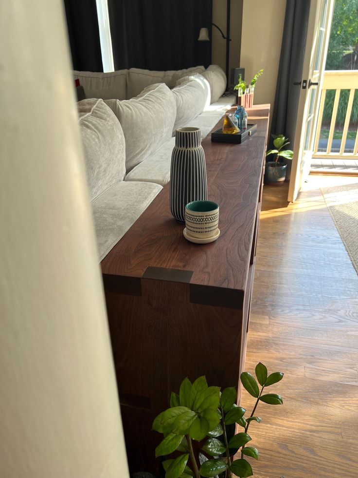 a living room filled with furniture and a wooden coffee table next to a plant in a vase