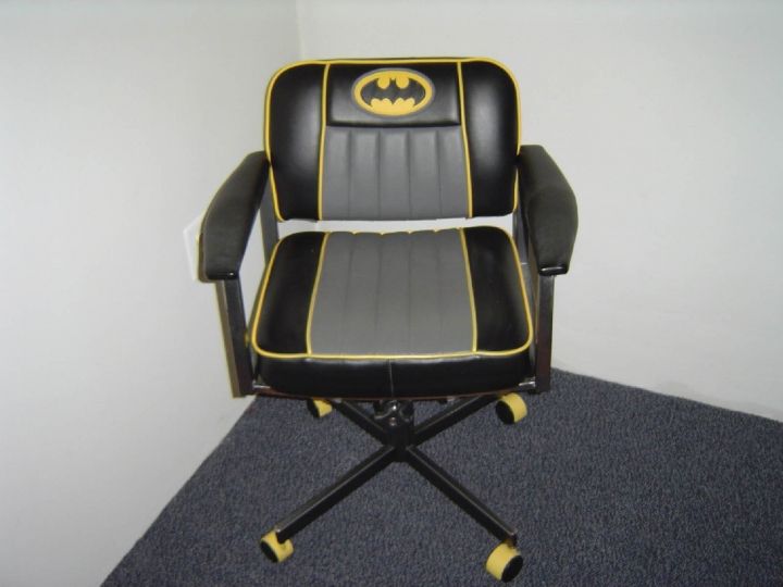 a black and yellow office chair with a batman symbol on the backrest, sitting in a corner