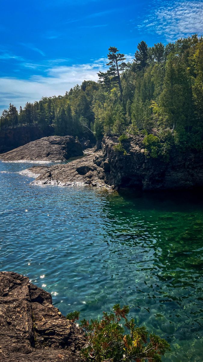 a body of water surrounded by trees on the side of a cliff with blue sky and clouds