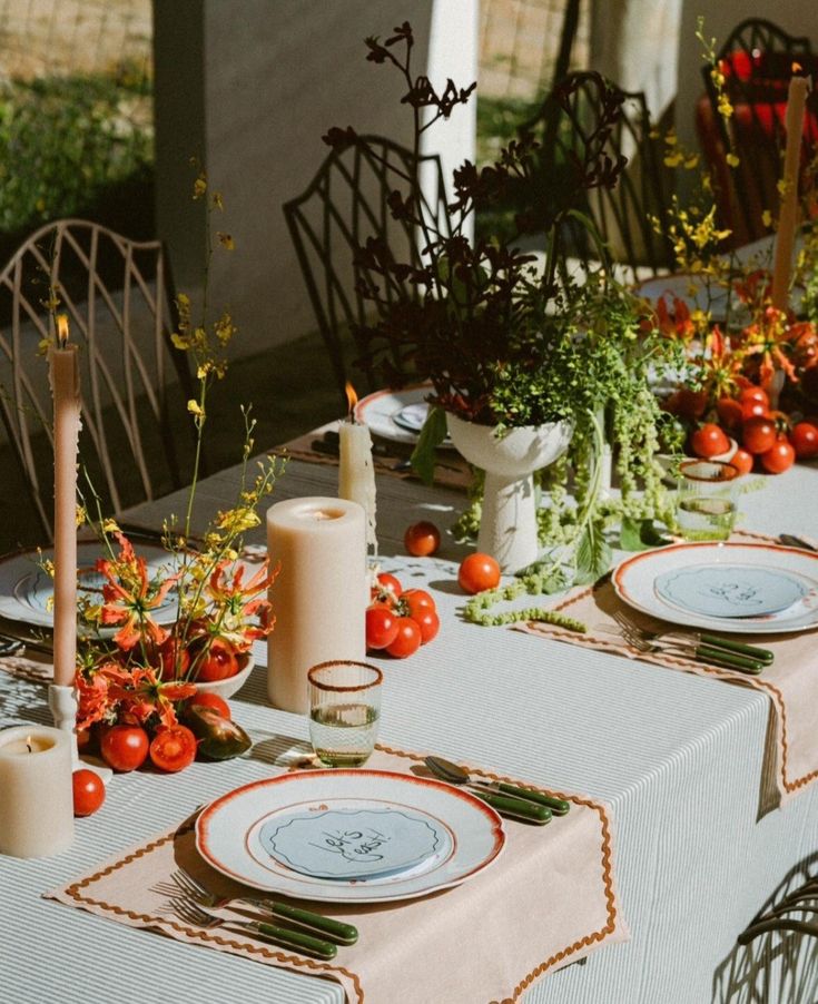 a table set with plates, candles and flowers on it for an outdoor dinner party