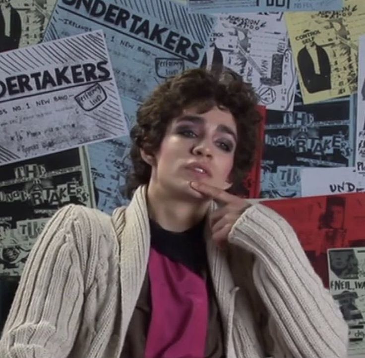 a young man sitting in front of a wall covered with newspaper clippings and posters