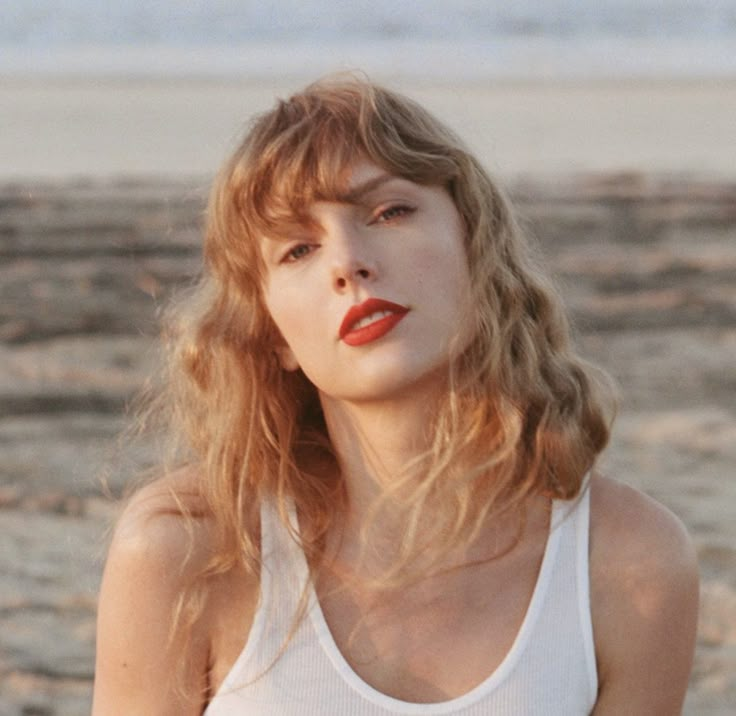 a woman standing on top of a sandy beach next to the ocean wearing a white tank top