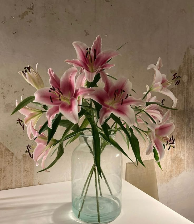 a vase filled with pink flowers sitting on top of a white table next to a wall