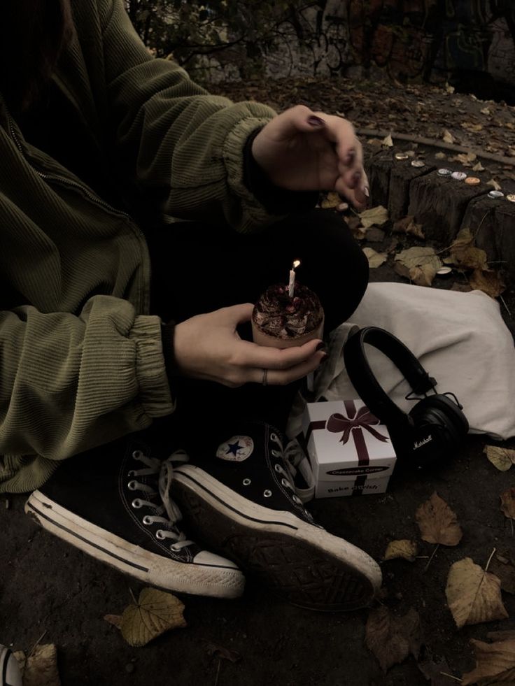 a woman sitting on the ground holding a small cake with a candle in her hand