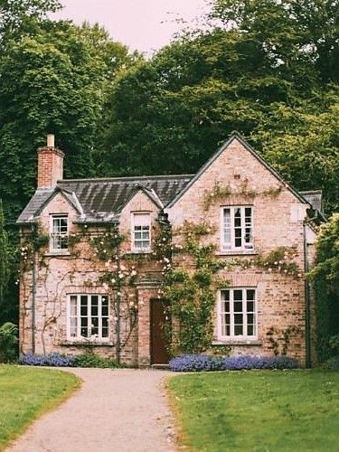 an old brick house with ivy growing on it's walls and windows, along side a path leading to the front door