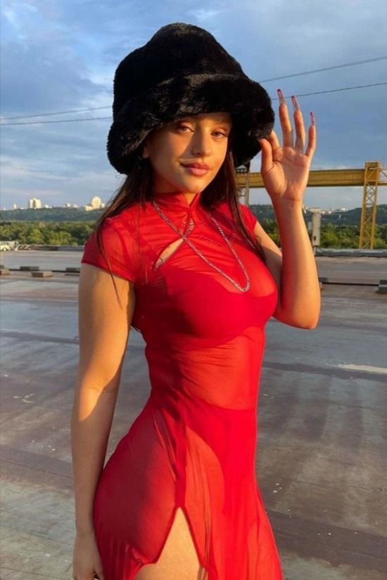 a woman in a red dress and black hat posing for the camera with her hand up