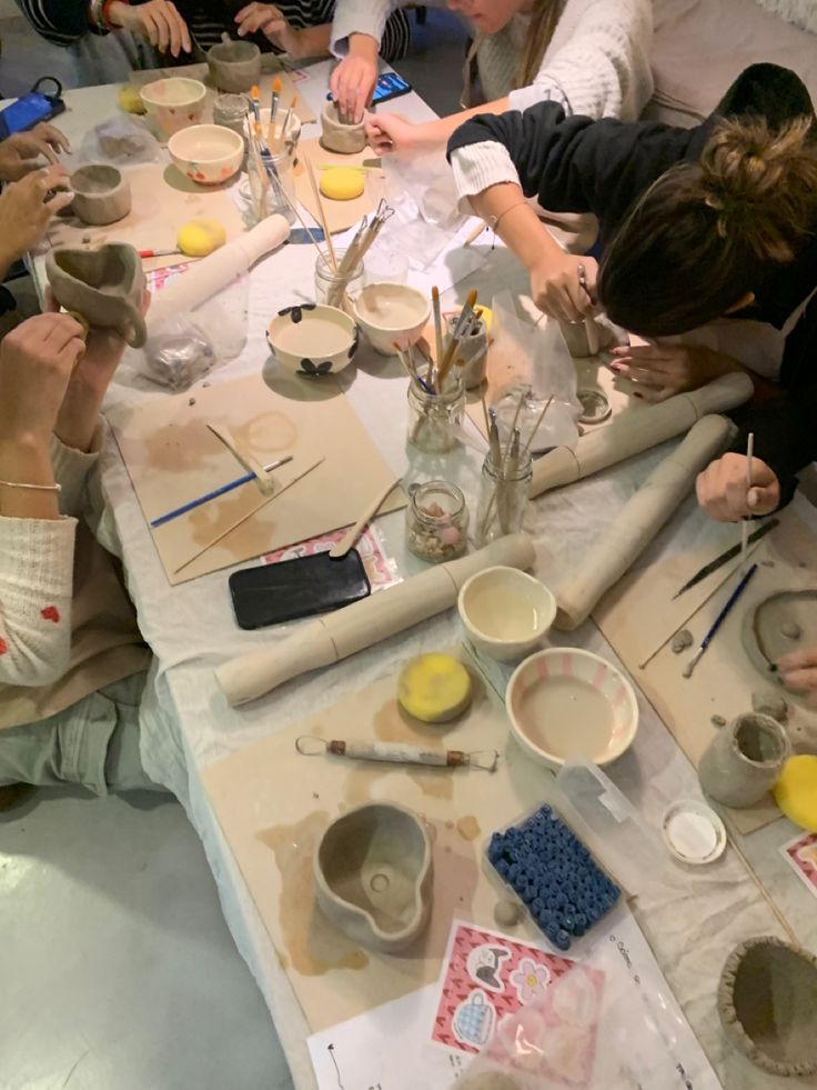 a group of people sitting around a table making bowls and spoons with paint on them