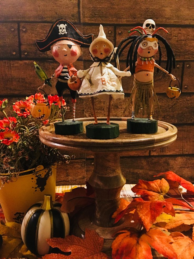 two figurines are sitting on top of a table with autumn leaves and pumpkins