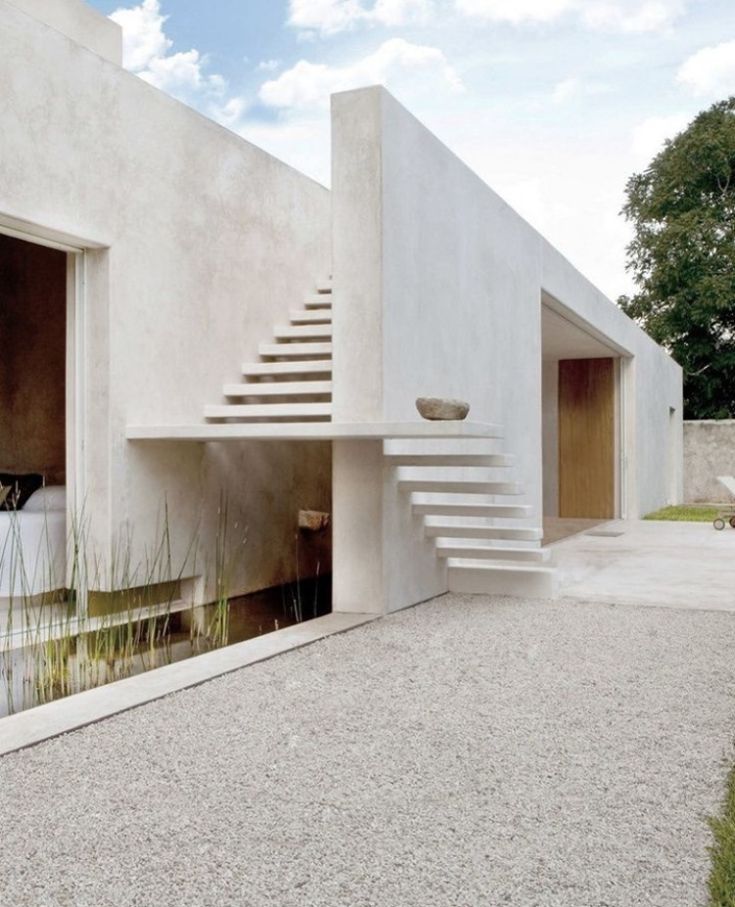 a white building with stairs leading up to it's entrance and water feature on the side