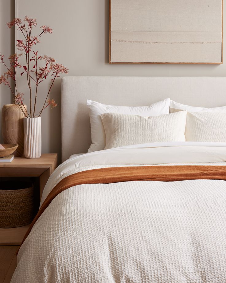 a bed with white linens and pillows in a small room next to a painting on the wall