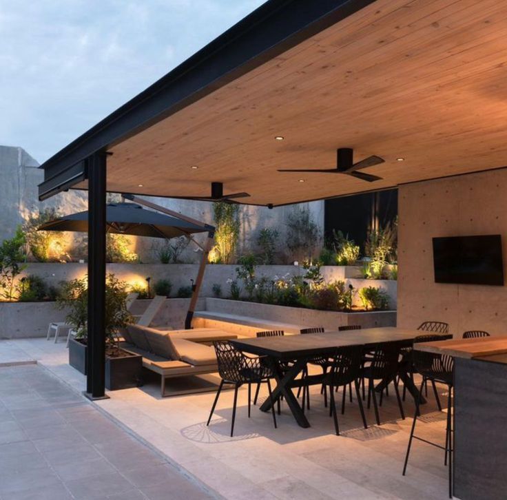 an outdoor dining area is lit up with lights and plants on the roof, along with seating for eight