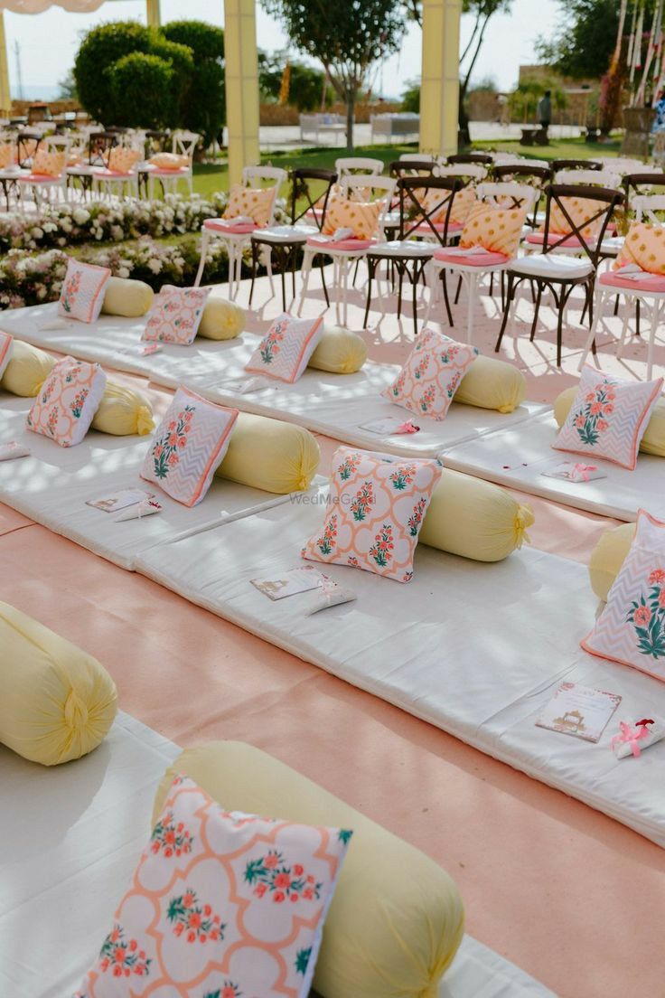 tables set up for an outdoor event with pink and yellow pillows