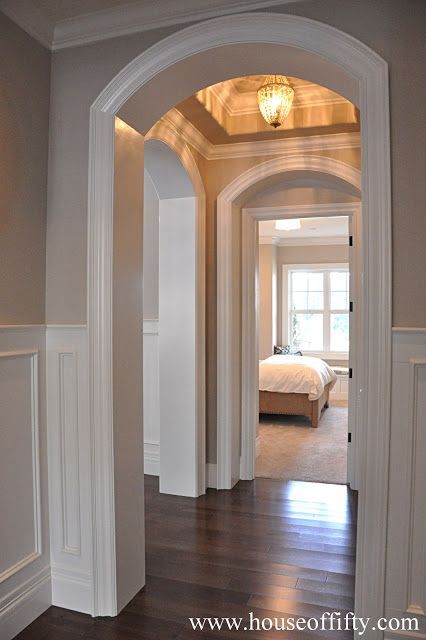 an archway leading to a bedroom with a bed in the background and hardwood flooring