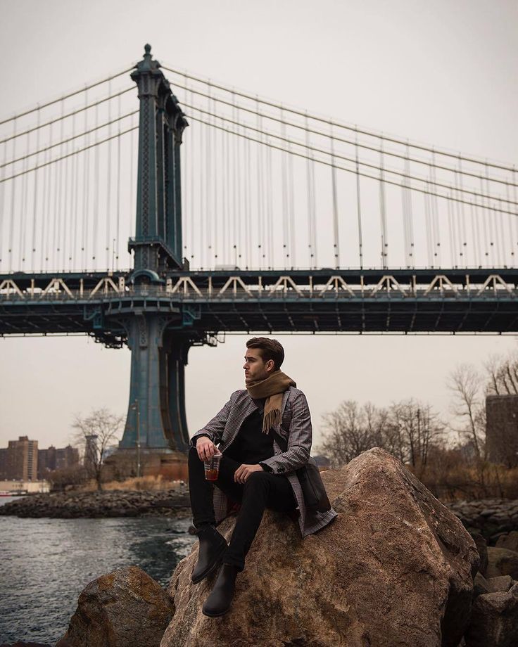 a man sitting on top of a rock next to a bridge