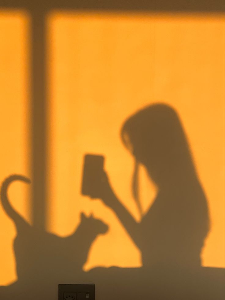 the shadow of a woman holding a cup in front of a cat on a table