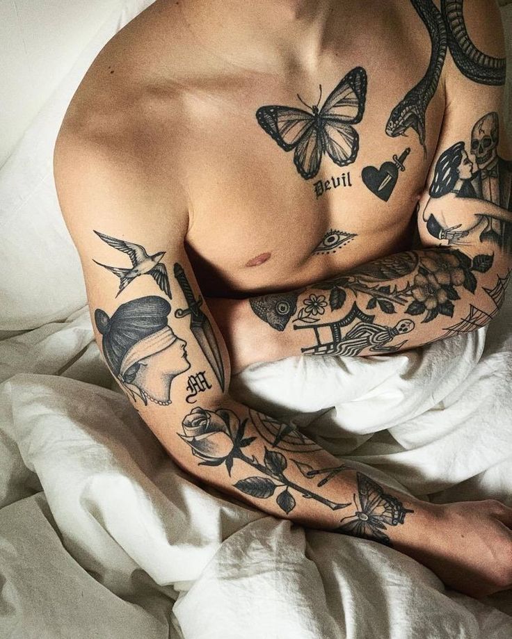 a man with tattoos on his arm and chest laying in bed next to white sheets