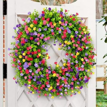 a colorful wreath is hanging on the side of a white gate with flowers all over it