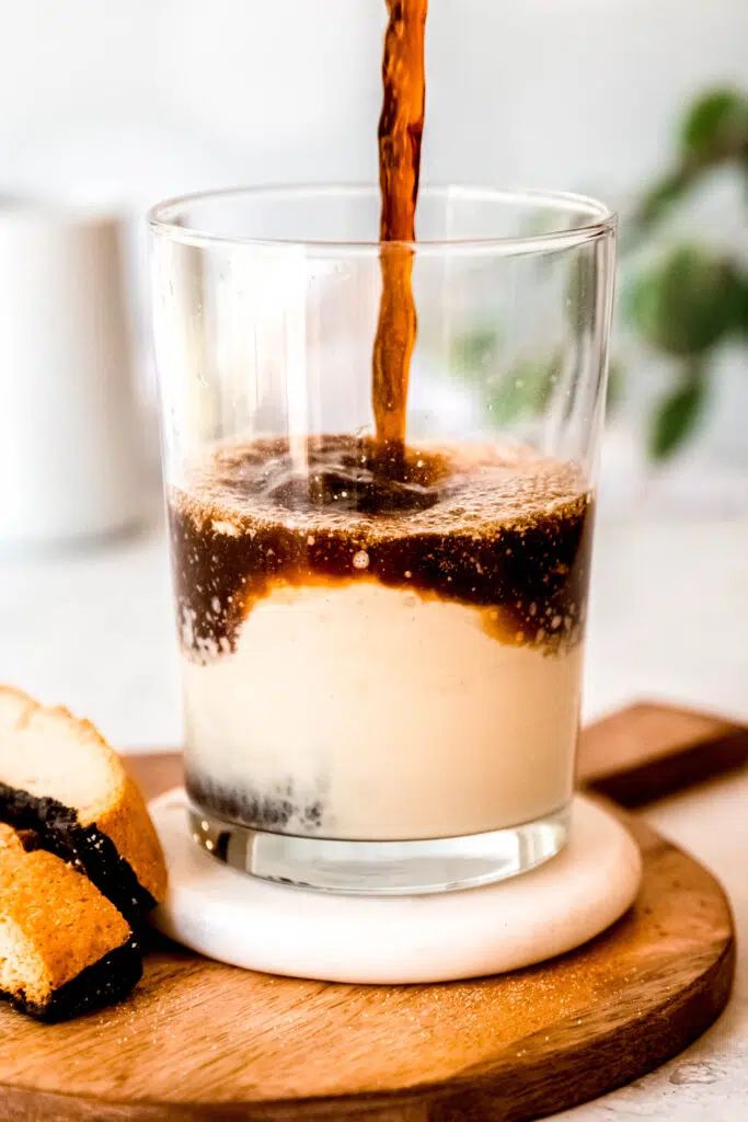 a glass filled with liquid sitting on top of a wooden cutting board next to a piece of bread