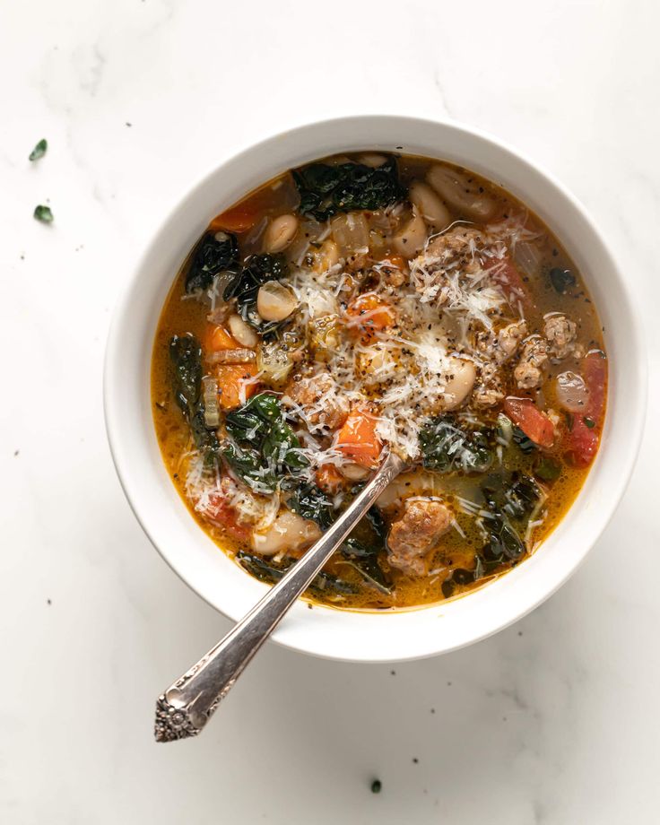 a bowl of soup with meat, vegetables and parmesan cheese on the top