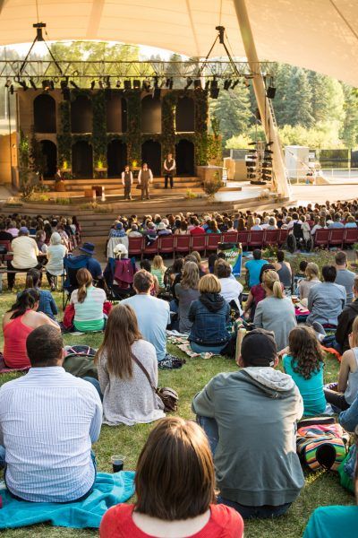 a group of people sitting on top of a lush green field next to a stage